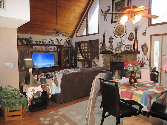 dining area featuring a stone fireplace, high vaulted ceiling, wood ceiling, ceiling fan, and light hardwood / wood-style floors