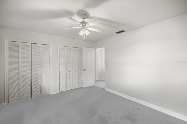 unfurnished bedroom with multiple closets, carpet floors, a textured ceiling, and ceiling fan