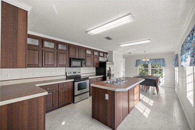 kitchen with sink, hanging light fixtures, stainless steel appliances, ornamental molding, and an island with sink