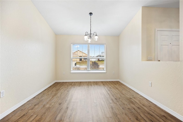 unfurnished dining area with vaulted ceiling, a notable chandelier, baseboards, and wood finished floors