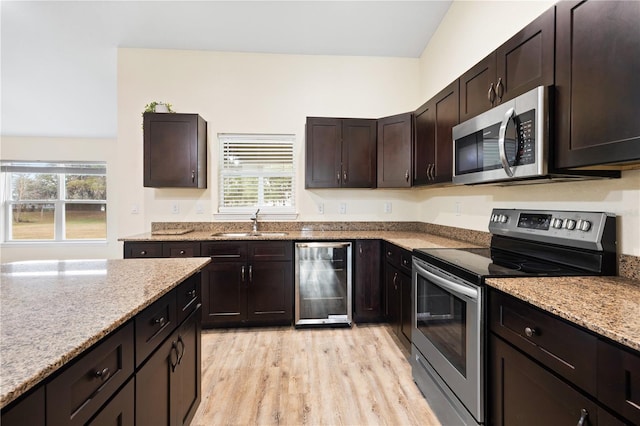 kitchen with a sink, light wood-type flooring, light stone counters, and appliances with stainless steel finishes