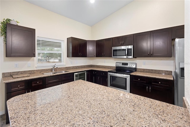 kitchen featuring dark brown cabinets, light stone counters, stainless steel appliances, high vaulted ceiling, and a sink