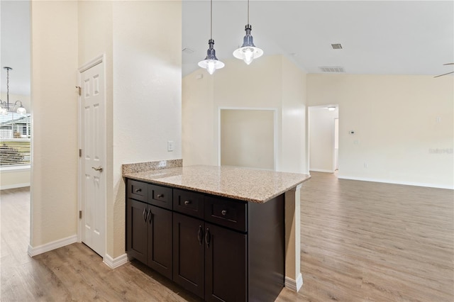 kitchen with light stone counters, visible vents, high vaulted ceiling, light wood-style flooring, and pendant lighting