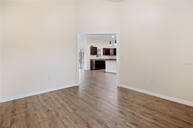 unfurnished room featuring baseboards, wood finished floors, and a towering ceiling