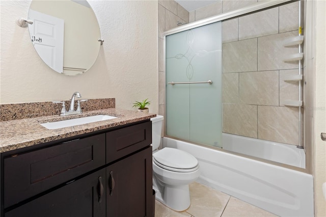 bathroom featuring tile patterned flooring, toilet, a textured wall, shower / bath combination with glass door, and vanity