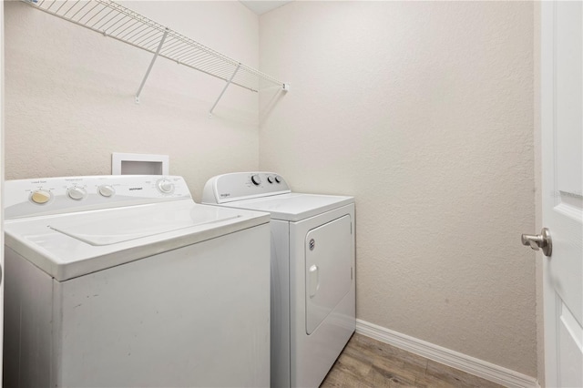 laundry room featuring baseboards, a textured wall, laundry area, light wood-style flooring, and washing machine and dryer