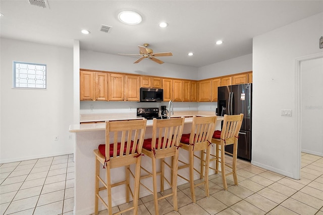 kitchen featuring light tile patterned floors, a kitchen breakfast bar, black appliances, and an island with sink