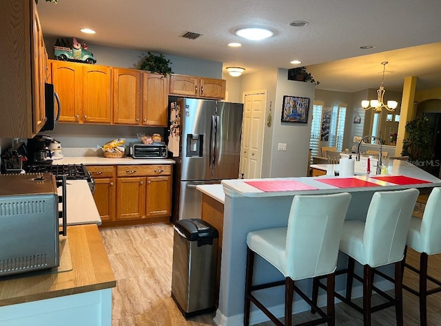 kitchen featuring stainless steel fridge, a kitchen bar, hanging light fixtures, a notable chandelier, and light hardwood / wood-style flooring