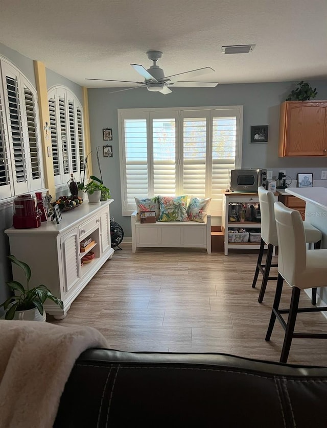 living room featuring ceiling fan, light hardwood / wood-style floors, and a textured ceiling