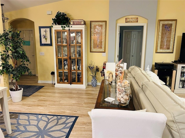 living room featuring arched walkways, baseboards, lofted ceiling, and light wood finished floors