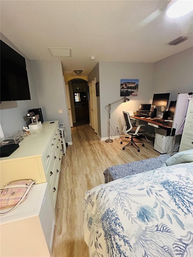 bedroom featuring arched walkways, visible vents, light wood-style flooring, and baseboards