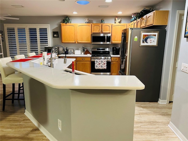 kitchen featuring light wood-style flooring, appliances with stainless steel finishes, a breakfast bar area, light countertops, and recessed lighting