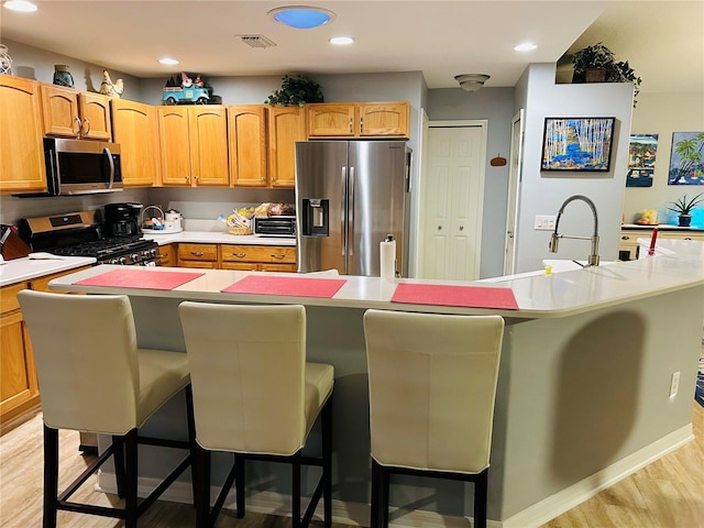 kitchen with an island with sink, light wood finished floors, appliances with stainless steel finishes, and a breakfast bar area