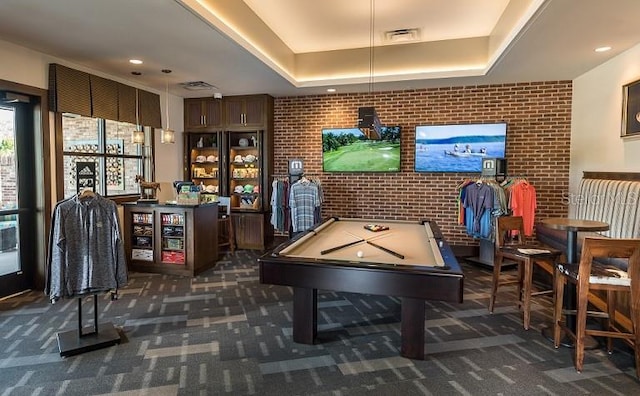 playroom with brick wall, a tray ceiling, and dark colored carpet