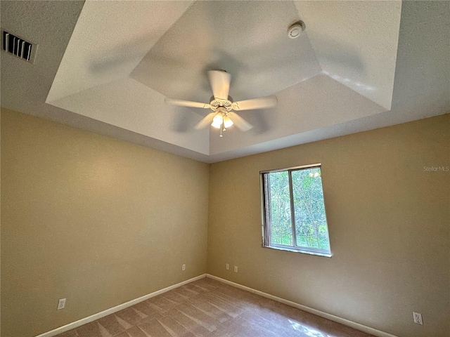 carpeted empty room with a tray ceiling and ceiling fan