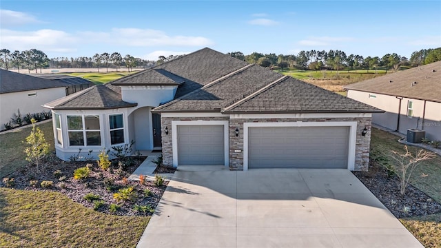 view of front of home with a shingled roof, central AC, a garage, stone siding, and driveway