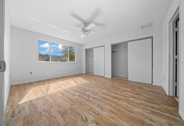 unfurnished bedroom featuring baseboards, multiple closets, wood finished floors, a textured ceiling, and a ceiling fan