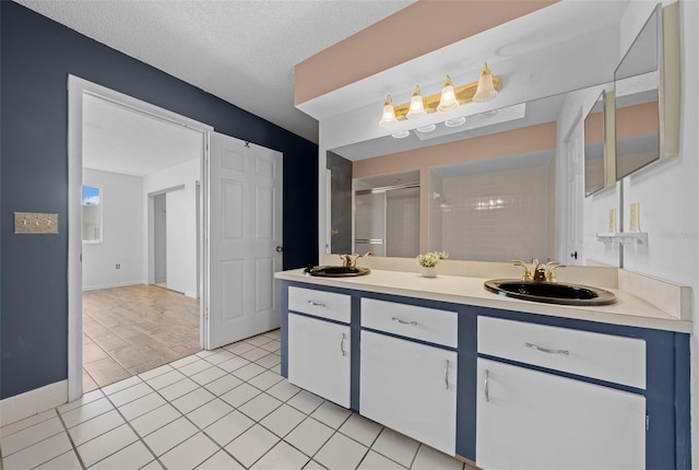 full bath with a textured ceiling, a shower stall, double vanity, and a sink