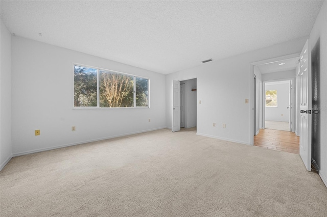 unfurnished bedroom with visible vents, light carpet, a textured ceiling, and baseboards