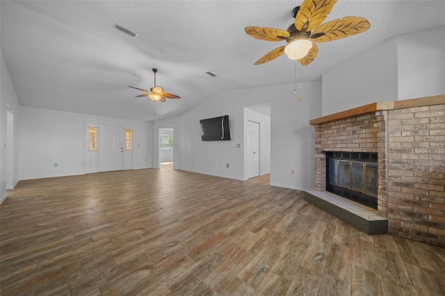 unfurnished living room with visible vents, vaulted ceiling, a fireplace, wood finished floors, and a ceiling fan