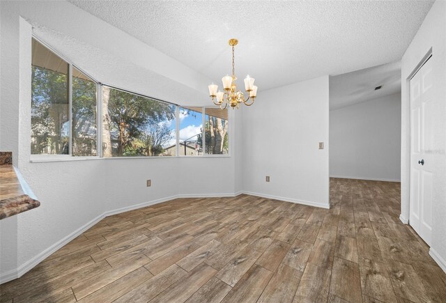 unfurnished dining area featuring baseboards, a textured ceiling, an inviting chandelier, and wood finished floors