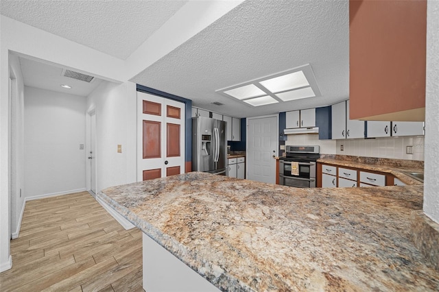 kitchen with visible vents, light wood-style flooring, a peninsula, a textured ceiling, and stainless steel appliances