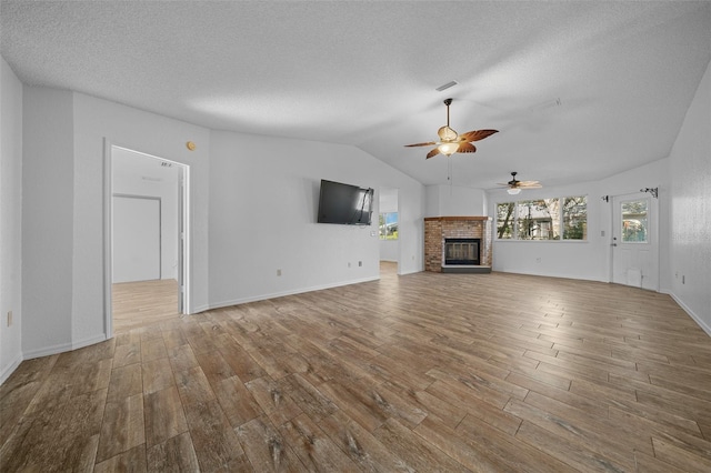 unfurnished living room with vaulted ceiling, a fireplace, a textured ceiling, and wood finished floors