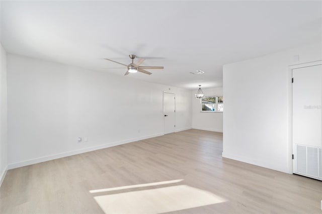 empty room featuring ceiling fan with notable chandelier and light wood-type flooring