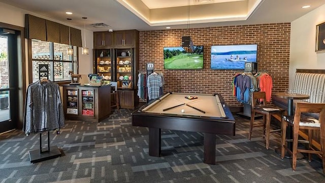 rec room with brick wall, a raised ceiling, and dark carpet