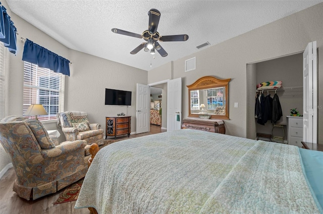 bedroom with ceiling fan, hardwood / wood-style floors, a textured ceiling, a walk in closet, and a closet