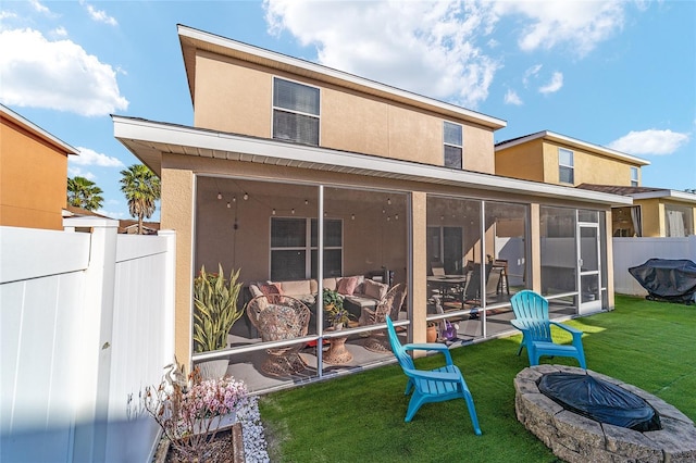 rear view of house featuring a sunroom, a yard, and an outdoor fire pit