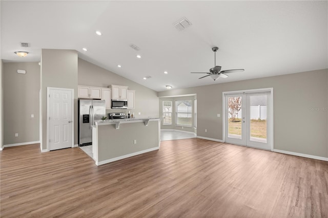 kitchen with a kitchen island, white cabinets, a kitchen breakfast bar, stainless steel appliances, and light wood-type flooring