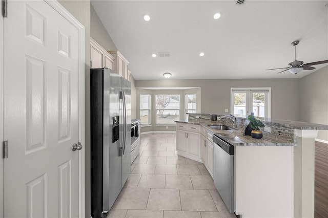 kitchen with light tile patterned flooring, sink, a large island with sink, stainless steel appliances, and white cabinets