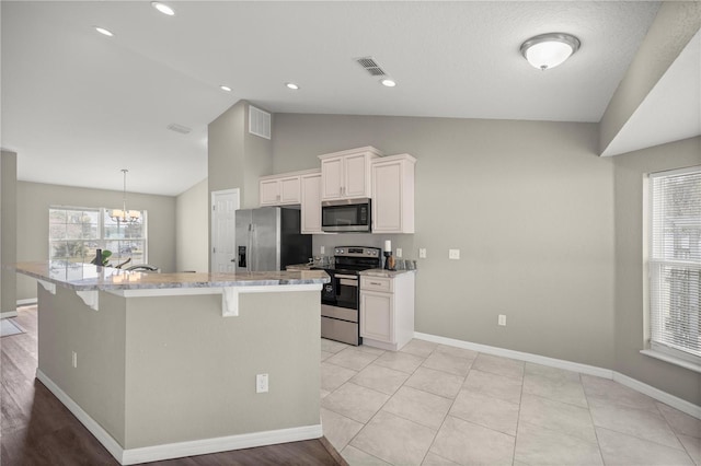 kitchen with white cabinetry, lofted ceiling, a kitchen breakfast bar, stainless steel appliances, and a spacious island