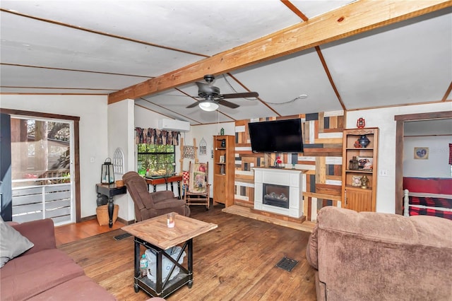 living room with a fireplace, vaulted ceiling with beams, an AC wall unit, ceiling fan, and hardwood / wood-style flooring