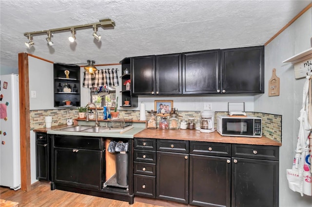 kitchen featuring dark cabinets, open shelves, a sink, and freestanding refrigerator