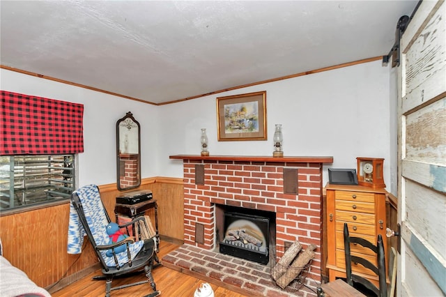 living area featuring ornamental molding, a brick fireplace, wainscoting, and wood finished floors