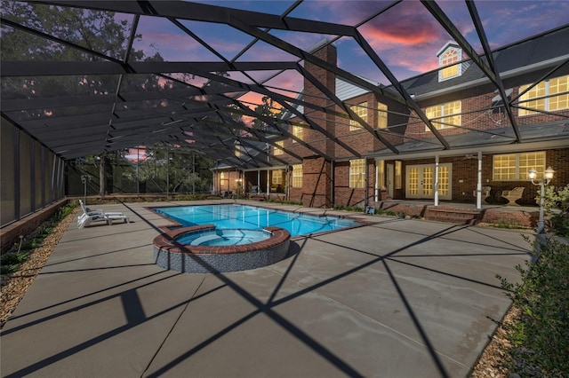 pool at dusk featuring an in ground hot tub, a lanai, and a patio area