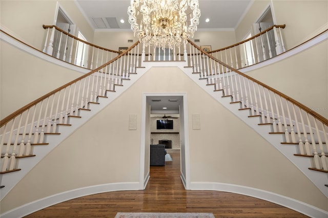 stairs with a high ceiling, ornamental molding, hardwood / wood-style floors, and a notable chandelier