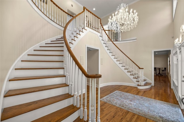 staircase featuring an inviting chandelier, a towering ceiling, ornamental molding, and hardwood / wood-style floors