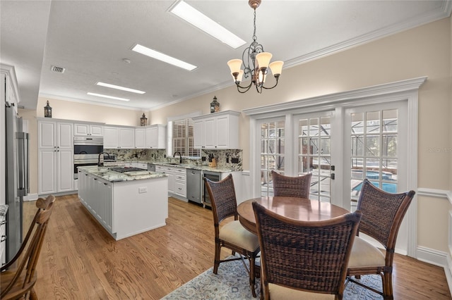 kitchen featuring white cabinetry, a center island, hanging light fixtures, stainless steel appliances, and light stone countertops