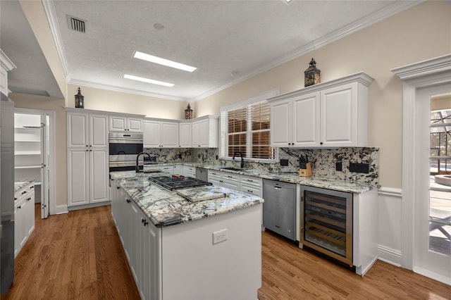 kitchen with appliances with stainless steel finishes, white cabinetry, a center island, wine cooler, and light stone countertops