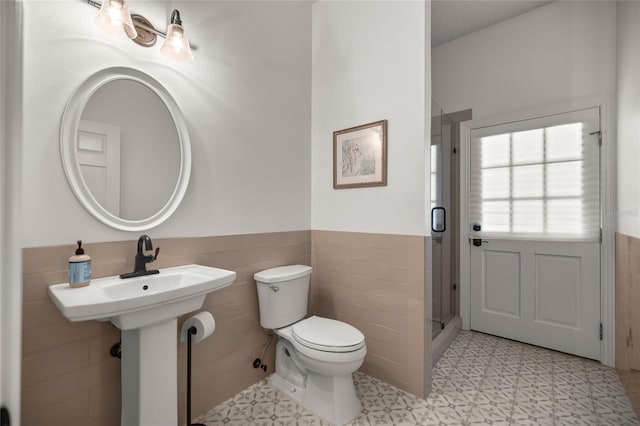 bathroom featuring tile walls, sink, a shower with door, and toilet