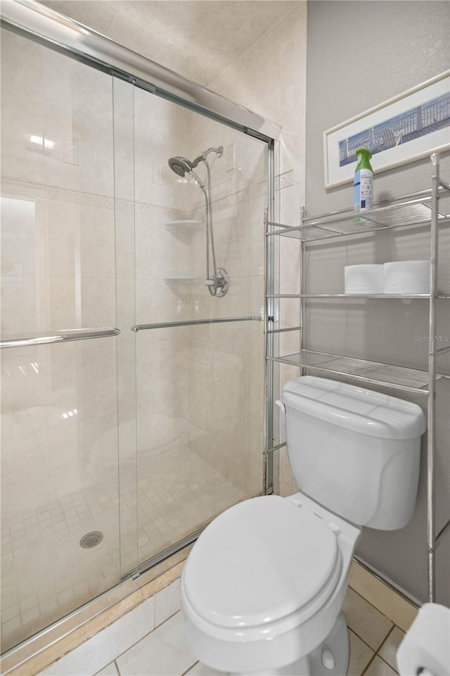 bathroom featuring toilet, an enclosed shower, and tile patterned flooring