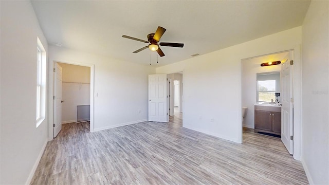 unfurnished bedroom with ensuite bath, a walk in closet, ceiling fan, light wood-type flooring, and a closet