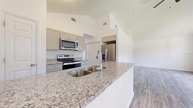 kitchen with sink, hardwood / wood-style flooring, ceiling fan, stainless steel appliances, and light stone countertops