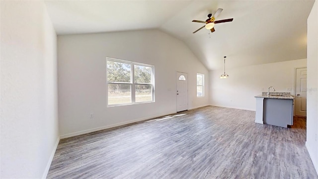 unfurnished living room featuring ceiling fan, wood-type flooring, sink, and vaulted ceiling