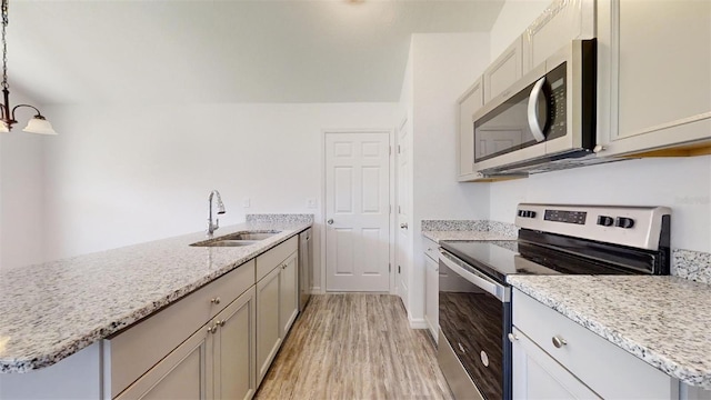 kitchen with pendant lighting, sink, light stone counters, light hardwood / wood-style floors, and stainless steel appliances