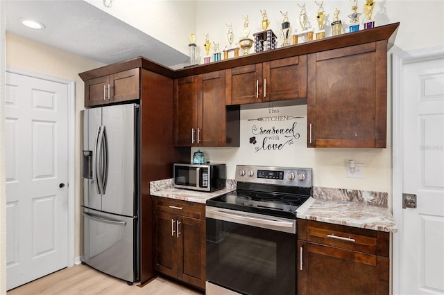 kitchen featuring dark brown cabinetry, appliances with stainless steel finishes, light stone counters, and light hardwood / wood-style floors