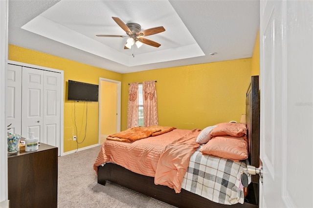 bedroom featuring a closet, carpet floors, ceiling fan, and a tray ceiling